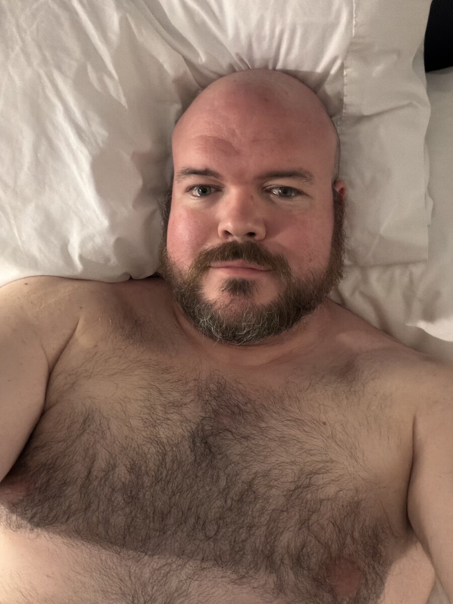 Sly Panorama press portrait — bald, full beard, dark wardrobe, studio lighting