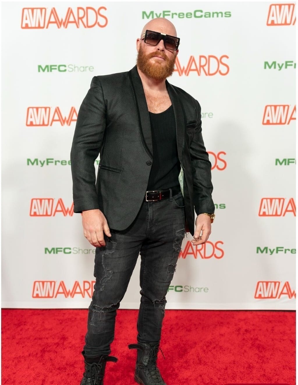 Thor Johnson on the AVN Awards red carpet, bald with a full red beard, charcoal blazer over a black v-neck and distressed jeans